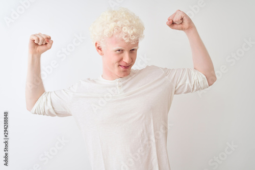 Young albino blond man wearing casual t-shirt standing over isolated white background showing arms muscles smiling proud. Fitness concept.