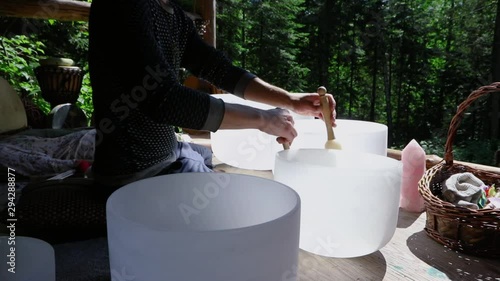 Diverse people enjoy spiritual gathering A shaman healer is seen rotating a sacred mallet around the rim of crystal alchemy singing bowls, creating acoustic vibration sounds believed to heal the body.