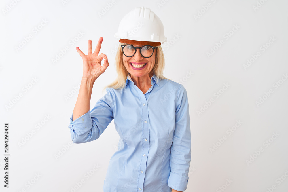 Middle age architect woman wearing glasses and helmet over isolated white background smiling positive doing ok sign with hand and fingers. Successful expression.
