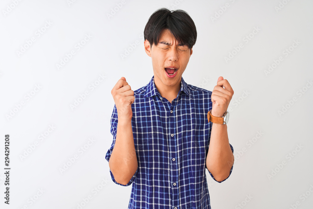 Young chinese man wearing casual blue shirt standing over isolated white background excited for success with arms raised and eyes closed celebrating victory smiling. Winner concept. Young chinese man wearing casual blue shirt standing over isolated white background excited for success with arms raised and eyes closed celebrating victory smiling. Winner concept.