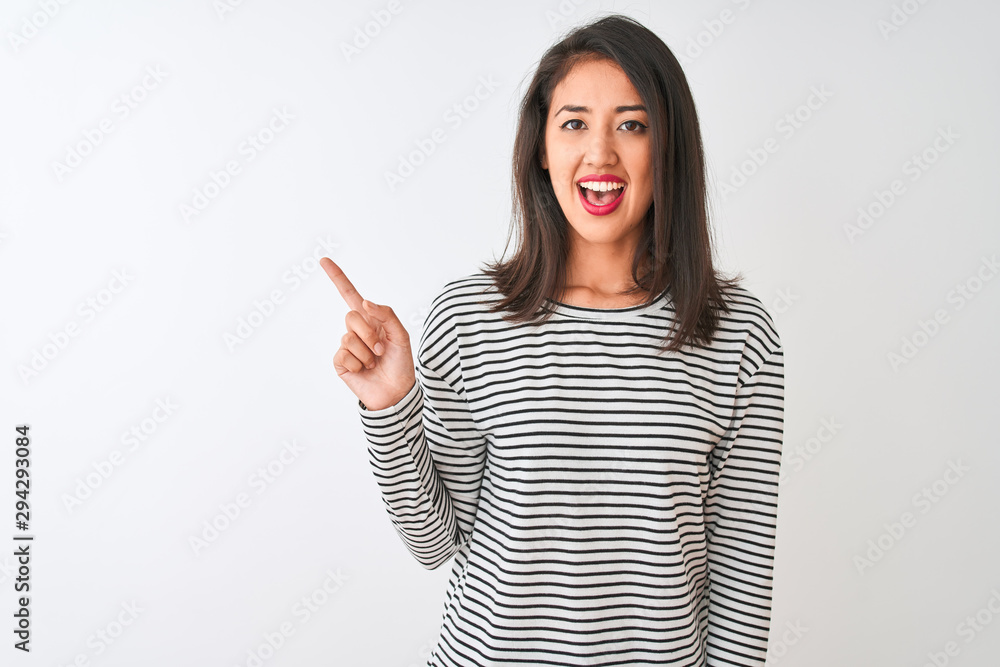 Young beautiful chinese woman wearing striped t-shirt standing over isolated white background with a big smile on face, pointing with hand and finger to the side looking at the camera. Young beautiful chinese woman wearing striped t-shirt standing over isolated white background with a big smile on face, pointing with hand and finger to the side looking at the camera.