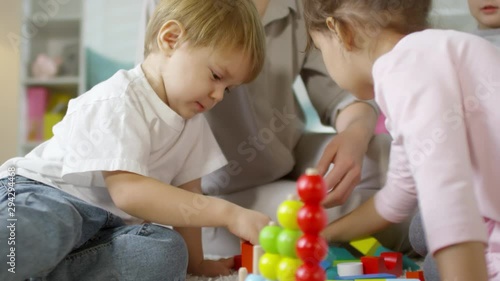 Close up view of cute little boy and girls sitting with female babysitter on the floor and playing with educational toy photo