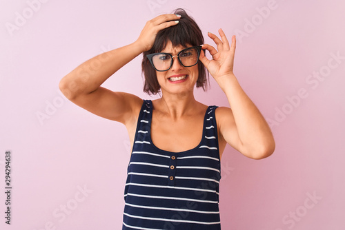Beautiful woman wearing striped t-shirt and glasses standing over isolated pink background stressed with hand on head, shocked with shame and surprise face, angry and frustrated. Fear