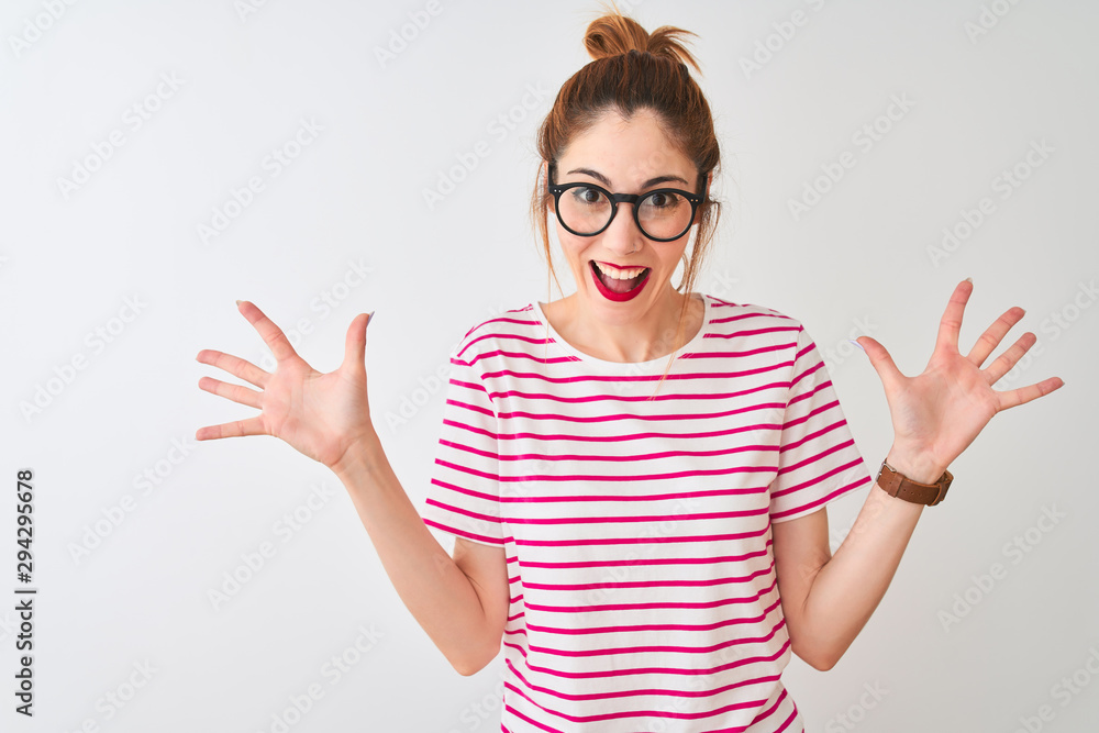 Redhead woman wearing glasses striped t-shirt and pigtail over isolated white background celebrating crazy and amazed for success with arms raised and open eyes screaming excited. Winner concept Redhead woman wearing glasses striped t-shirt and pigtail over isolated white background celebrating crazy and amazed for success with arms raised and open eyes screaming excited. Winner concept