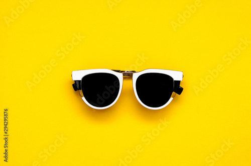 White sunglasses with black lenses glasses on a bright colorful yellow background. Flat Lay