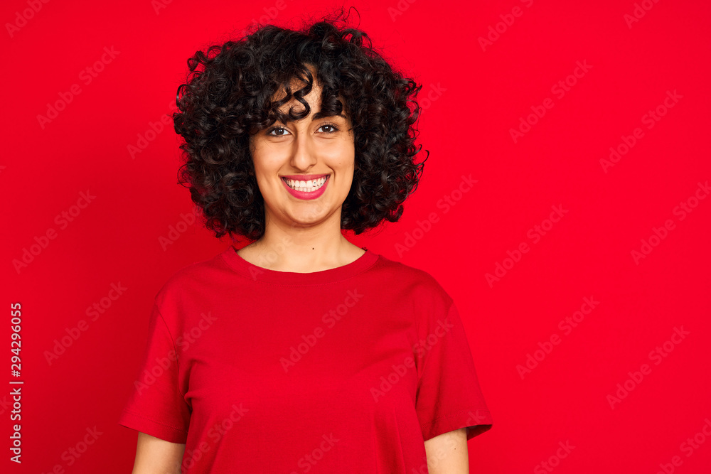 Young arab woman with curly hair wearing casual t-shirt over isolated red background with a happy and cool smile on face. Lucky person. Young arab woman with curly hair wearing casual t-shirt over isolated red background with a happy and cool smile on face. Lucky person.