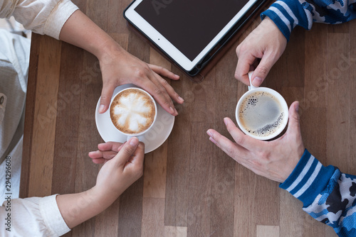 Couple hand  holding hot coffee cup on wooden table.Business man and woman drinking espresso and latte art menu with tablet and mobile phone in the restaurant.Lover  in coffee shop.