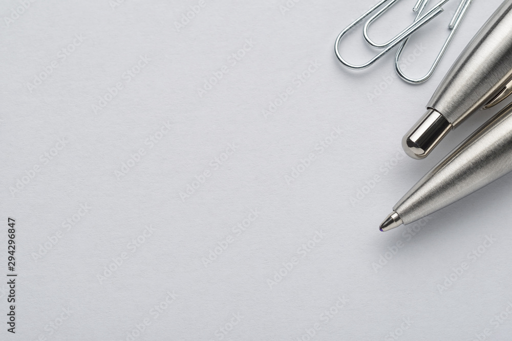 Metal ballpoint pen and paper clips on white paper