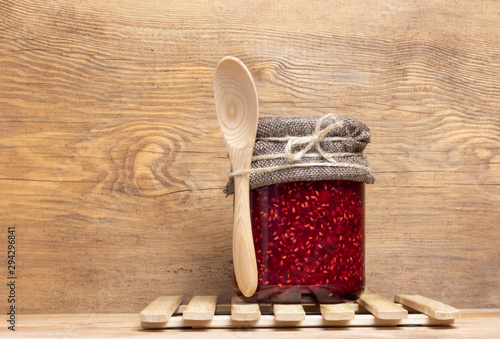 jar with raspberry jam stands on a wooden background