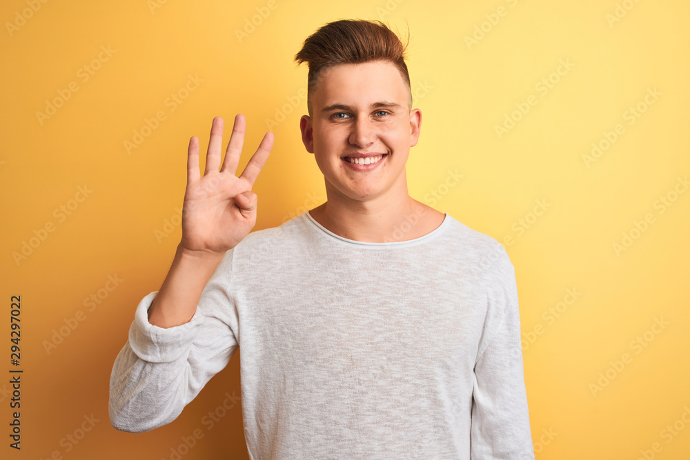 Young handsome man wearing white casual t-shirt standing over isolated yellow background showing and pointing up with fingers number four while smiling confident and happy. Young handsome man wearing white casual t-shirt standing over isolated yellow background showing and pointing up with fingers number four while smiling confident and happy.