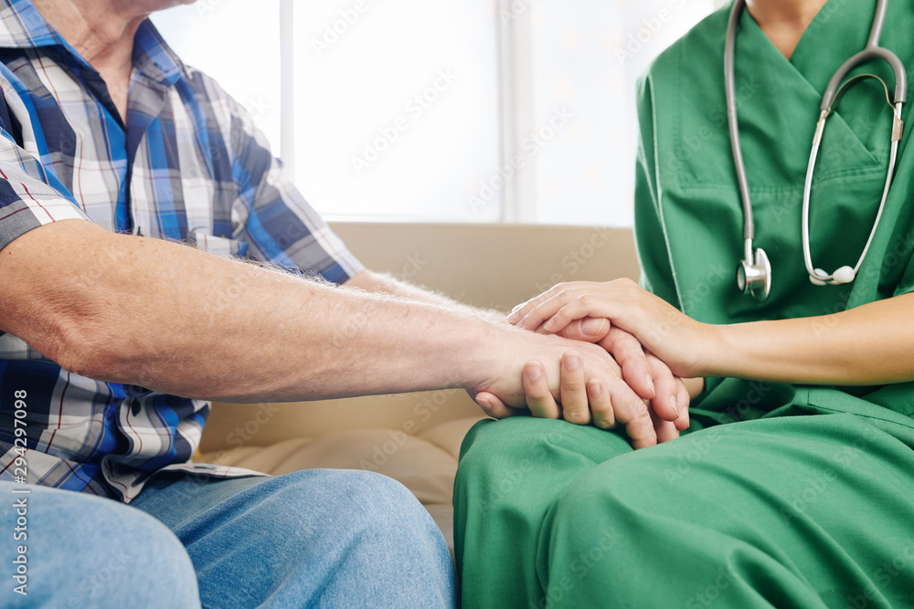 Close-up image of caregiver holding hands of elderly patient to comfort him during home visit Close-up image of caregiver holding hands of elderly patient to comfort him during home visit