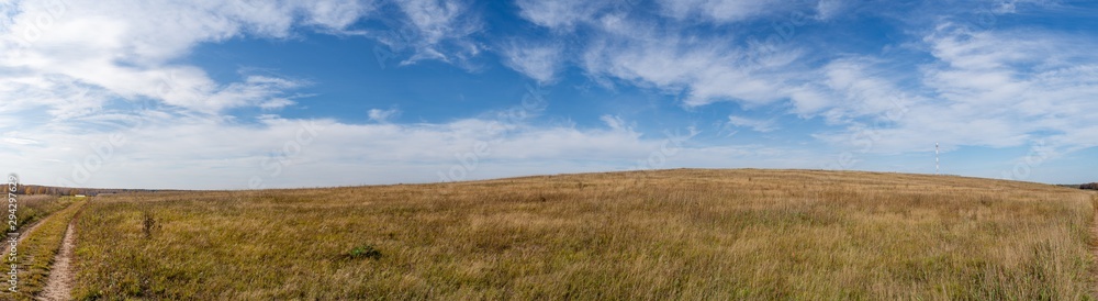 Panorama of a hilly field with a dirt road and a communication tower