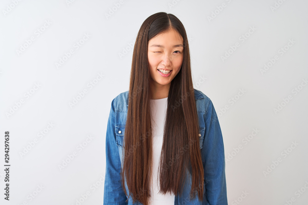Young chinese woman wearing denim shirt standing over isolated white background winking looking at the camera with sexy expression, cheerful and happy face. Young chinese woman wearing denim shirt standing over isolated white background winking looking at the camera with sexy expression, cheerful and happy face.