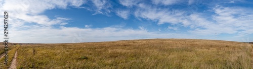 Panorama of a hilly field with a dirt road and a communication tower