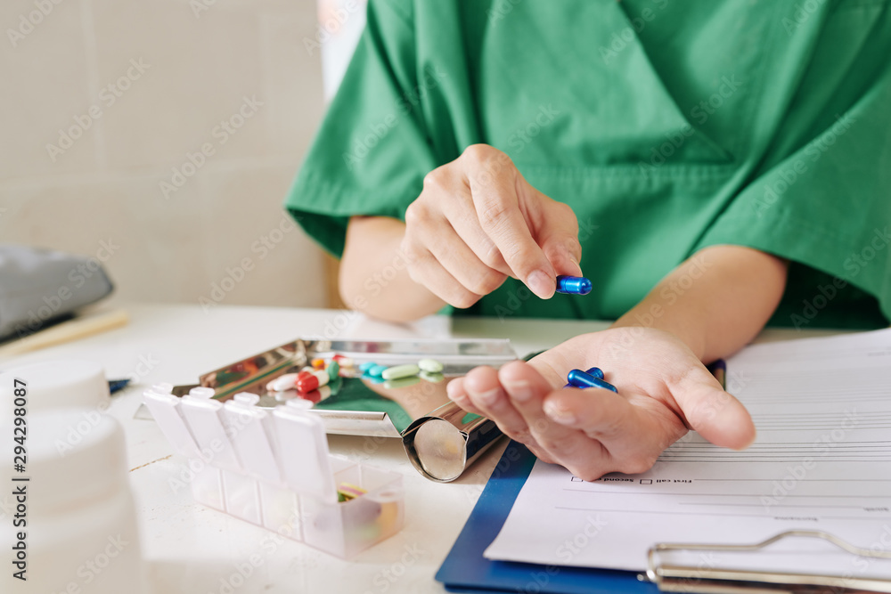Hands of nurse putting prescribed pills for patient in metal plate