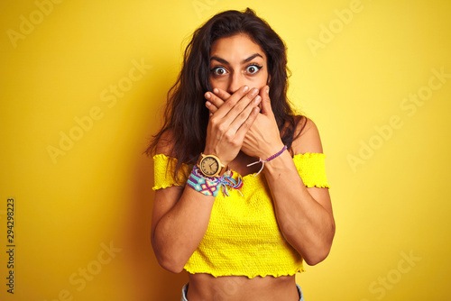 Young beautiful woman wearing casual t-shirt standing over isolated yellow background shocked covering mouth with hands for mistake. Secret concept.