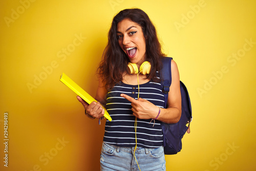 Student woman wearing bakcpack notebook headphones over isolated yellow background very happy pointing with hand and finger