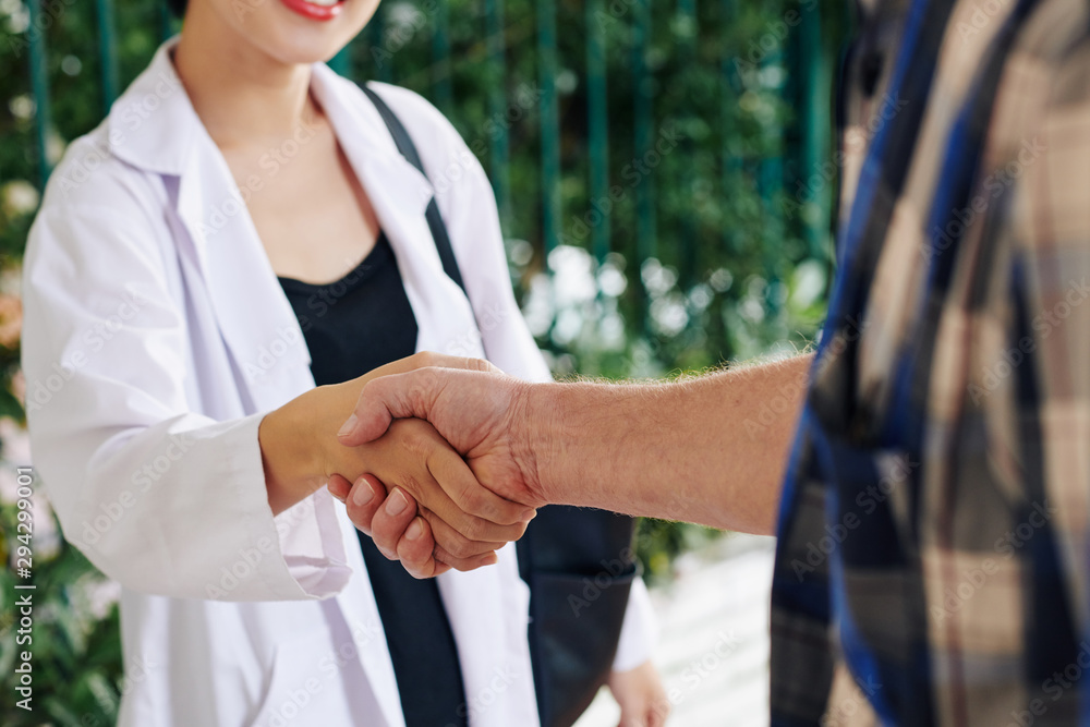Close-up image of hospital worker and senior patient shaking hands after discussing prescription and therapy