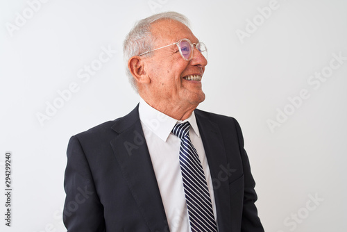 Senior grey-haired businessman wearing suit and glasses over isolated white background looking away to side with smile on face, natural expression. Laughing confident.