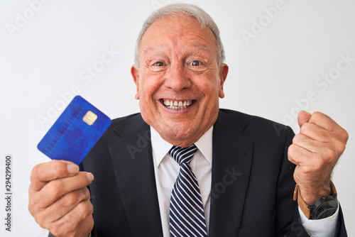 Senior grey-haired businessman holding credit card over isolated white background screaming proud and celebrating victory and success very excited, cheering emotion © Krakenimages.com