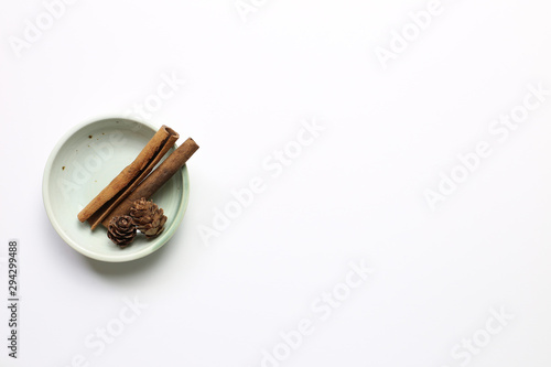 Pine cones and cinnamon sticks in a bowl on white background. Autumn concept