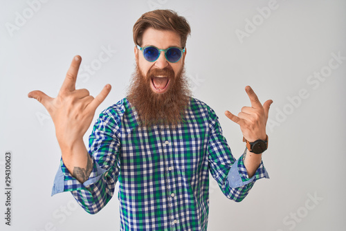 Young redhead irish man wearing casual shirt and sunglasses over isolated white background shouting with crazy expression doing rock symbol with hands up. Music star. Heavy concept.