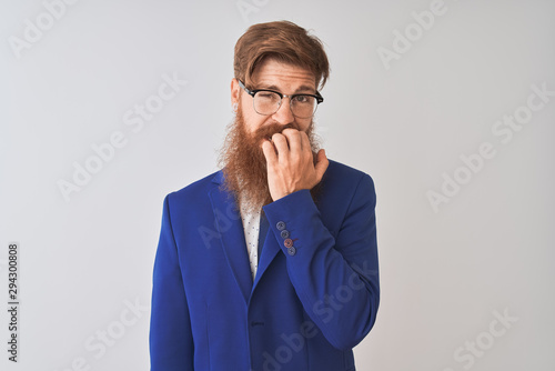 Young redhead irish businessman wearing suit and glasses over isolated white background looking stressed and nervous with hands on mouth biting nails. Anxiety problem.