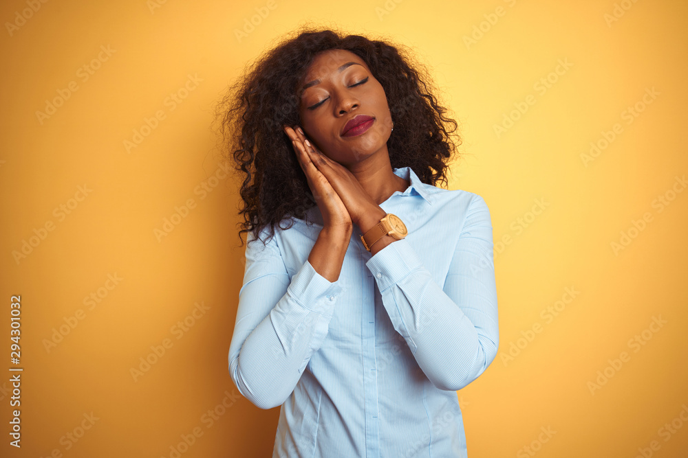 African american businesswoman wearing elegant shirt over isolated yellow background sleeping tired dreaming and posing with hands together while smiling with closed eyes. African american businesswoman wearing elegant shirt over isolated yellow background sleeping tired dreaming and posing with hands together while smiling with closed eyes.