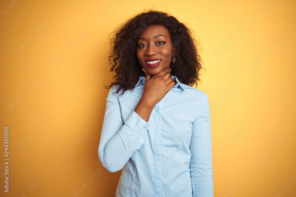 African american businesswoman wearing elegant shirt over isolated yellow background looking confident at the camera smiling with crossed arms and hand raised on chin. Thinking positive. African american businesswoman wearing elegant shirt over isolated yellow background looking confident at the camera smiling with crossed arms and hand raised on chin. Thinking positive.