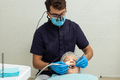 Yoing boy got his tooth drilled by stomatologist wearing gloves and microscope glasses photo