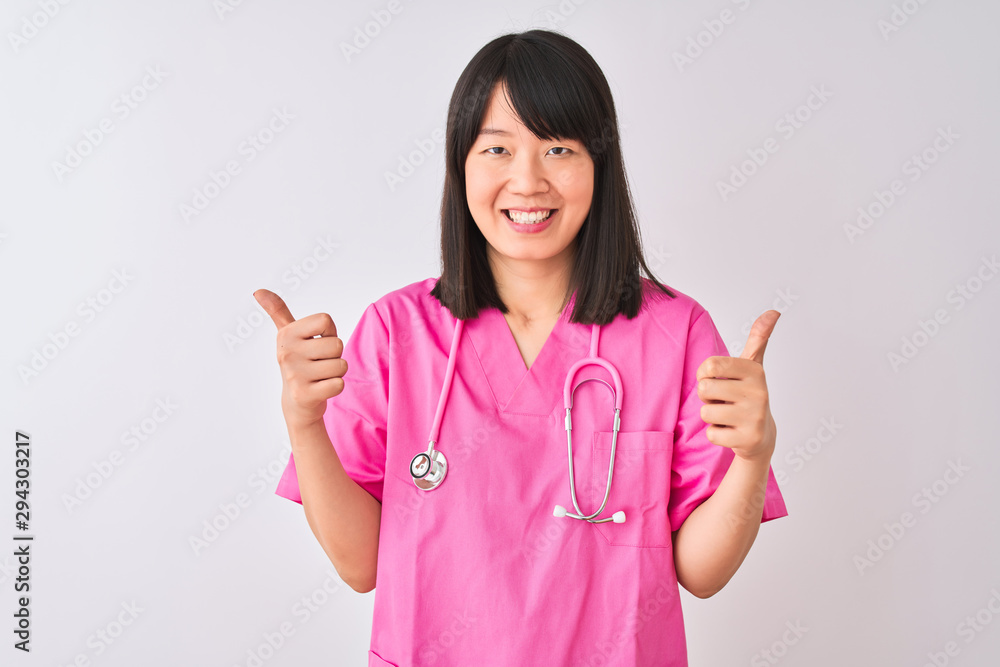 Young beautiful Chinese nurse woman wearing stethoscope over isolated white background success sign doing positive gesture with hand, thumbs up smiling and happy. Cheerful expression Young beautiful Chinese nurse woman wearing stethoscope over isolated white background success sign doing positive gesture with hand, thumbs up smiling and happy. Cheerful expression