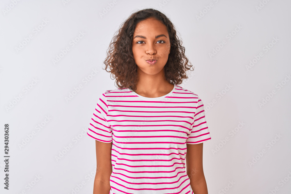 Young brazilian woman wearing pink striped t-shirt standing over isolated white background puffing cheeks with funny face. Mouth inflated with air, crazy expression. Young brazilian woman wearing pink striped t-shirt standing over isolated white background puffing cheeks with funny face. Mouth inflated with air, crazy expression.