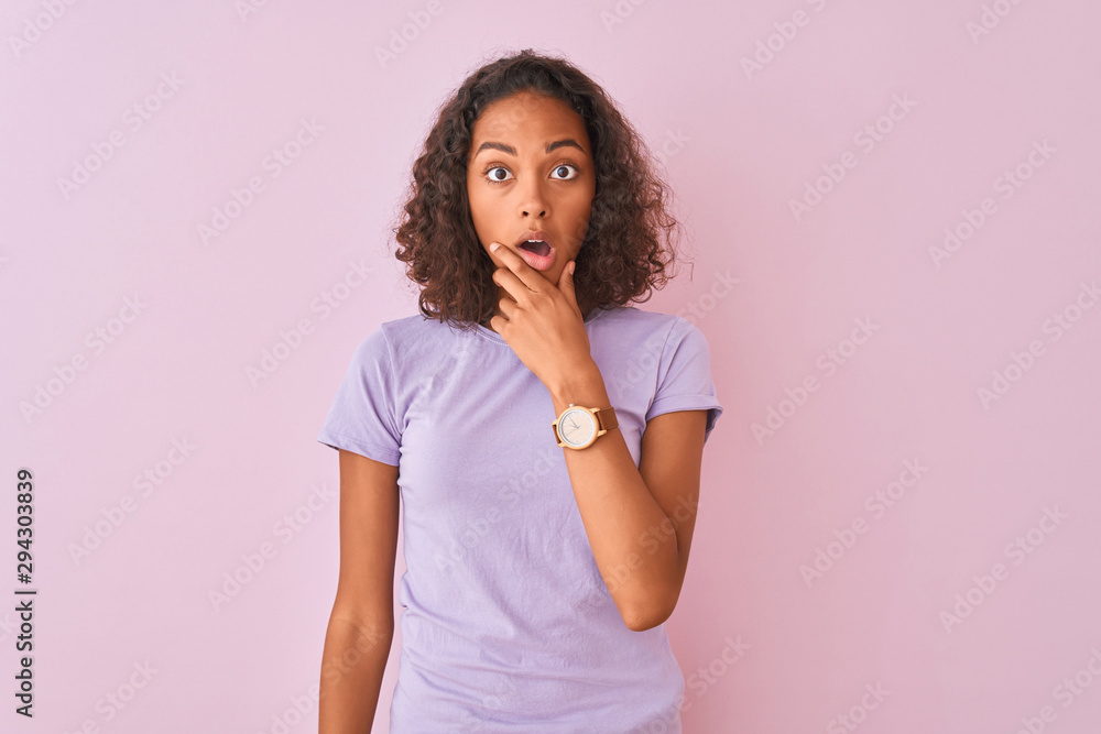 Young brazilian woman wearing t-shirt standing over isolated pink background Looking fascinated with disbelief, surprise and amazed expression with hands on chin Young brazilian woman wearing t-shirt standing over isolated pink background Looking fascinated with disbelief, surprise and amazed expression with hands on chin