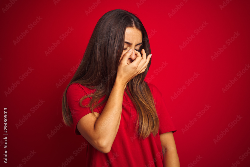 Young beautiful woman wearing t-shirt standing over isolated red background tired rubbing nose and eyes feeling fatigue and headache. Stress and frustration concept. Young beautiful woman wearing t-shirt standing over isolated red background tired rubbing nose and eyes feeling fatigue and headache. Stress and frustration concept.