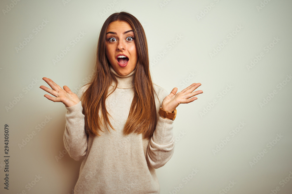 Young beautiful woman wearing winter turtleneck sweater over isolated white background celebrating crazy and amazed for success with arms raised and open eyes screaming excited. Winner concept Young beautiful woman wearing winter turtleneck sweater over isolated white background celebrating crazy and amazed for success with arms raised and open eyes screaming excited. Winner concept