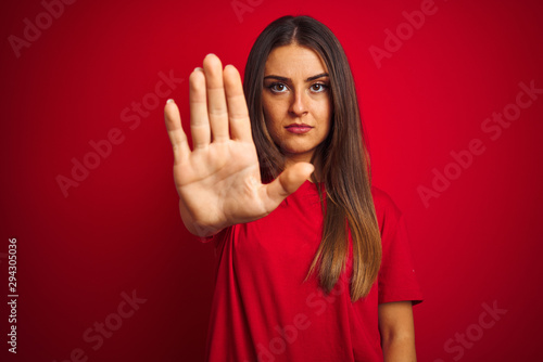 Young beautiful woman wearing t-shirt standing over isolated red background doing stop sing with palm of the hand. Warning expression with negative and serious gesture on the face.