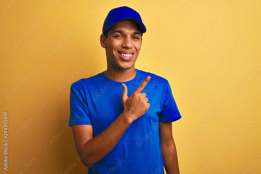Young handsome arab delivery man standing over isolated yellow background cheerful with a smile of face pointing with hand and finger up to the side with happy and natural expression on face Young handsome arab delivery man standing over isolated yellow background cheerful with a smile of face pointing with hand and finger up to the side with happy and natural expression on face