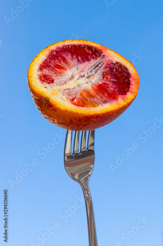 Bild auf Leinwand A slice of red orange, impaled on a metal fork on a blue background, close-up