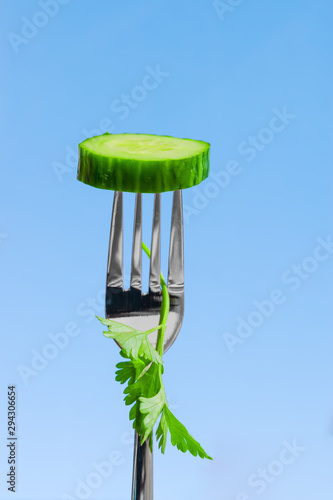 Quadro su tela A slice of green cucumber, impaled on a metal fork on a blue background, close-u