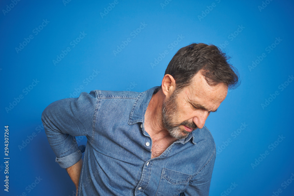 Handsome middle age senior man with grey hair over isolated blue background Suffering of backache, touching back with hand, muscular pain Handsome middle age senior man with grey hair over isolated blue background Suffering of backache, touching back with hand, muscular pain