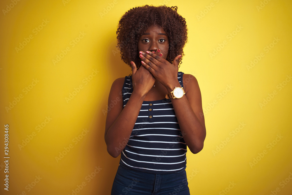 Young african afro woman wearing striped t-shirt over isolated yellow background shocked covering mouth with hands for mistake. Secret concept. Young african afro woman wearing striped t-shirt over isolated yellow background shocked covering mouth with hands for mistake. Secret concept.