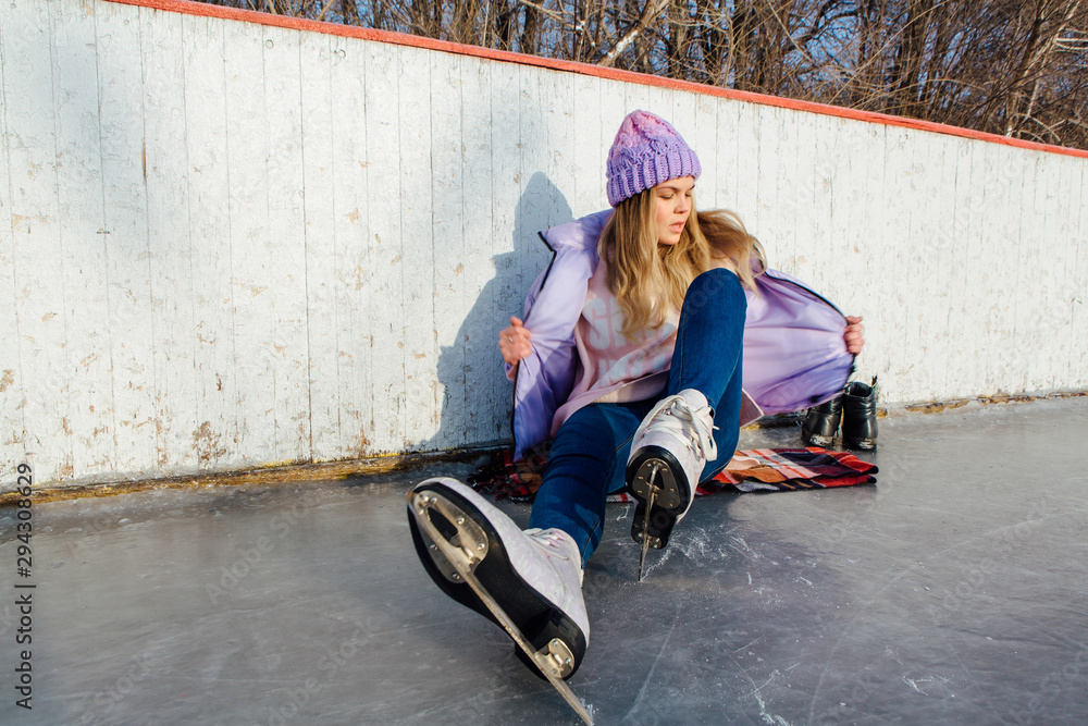 Lovely young woman sitting on ice ring and tieing shoelaces Lovely young woman sitting on ice ring and tieing shoelaces