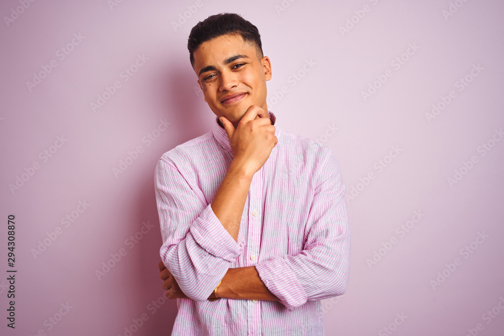 Young brazilian man wearing shirt standing over isolated pink background looking confident at the camera smiling with crossed arms and hand raised on chin. Thinking positive. Young brazilian man wearing shirt standing over isolated pink background looking confident at the camera smiling with crossed arms and hand raised on chin. Thinking positive.