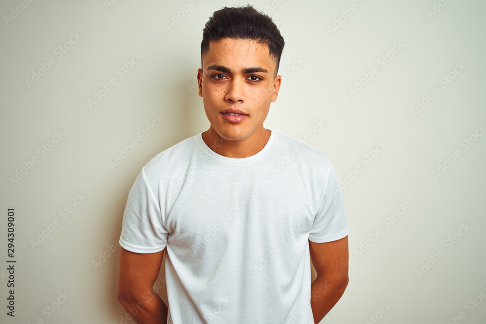Young brazilian man wearing t-shirt standing over isolated white background with serious expression on face. Simple and natural looking at the camera. Young brazilian man wearing t-shirt standing over isolated white background with serious expression on face. Simple and natural looking at the camera.