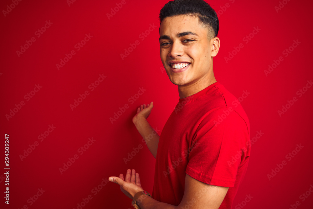 Young brazilian man wearing t-shirt standing over isolated red background Inviting to enter smiling natural with open hand Young brazilian man wearing t-shirt standing over isolated red background Inviting to enter smiling natural with open hand