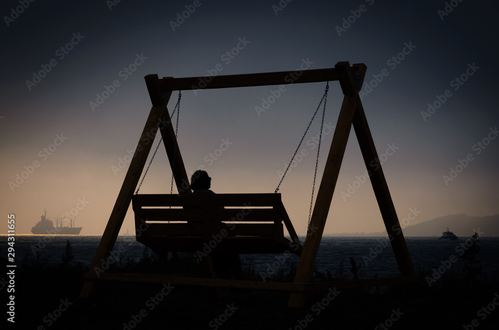 Silhouette of a woman on a swing by the sea in the evening Silhouette of a woman on a swing by the sea in the evening