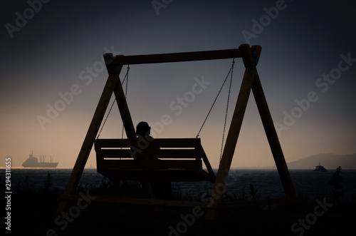 Silhouette of a woman on a swing by the sea in the evening