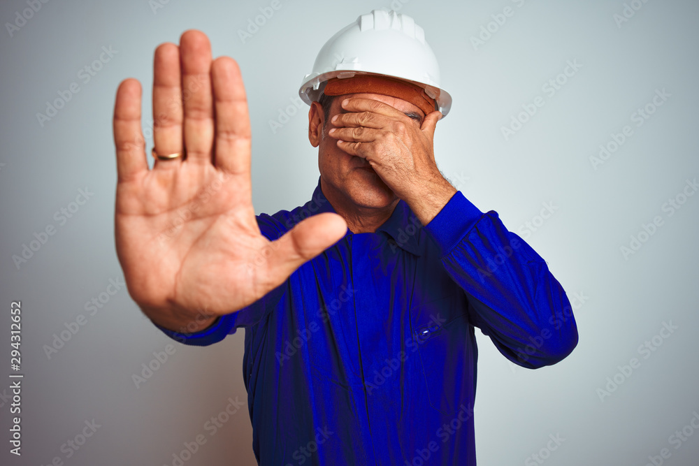 Handsome middle age worker man wearing uniform and helmet over isolated white background covering eyes with hands and doing stop gesture with sad and fear expression. Embarrassed and negative concept. Handsome middle age worker man wearing uniform and helmet over isolated white background covering eyes with hands and doing stop gesture with sad and fear expression. Embarrassed and negative concept.