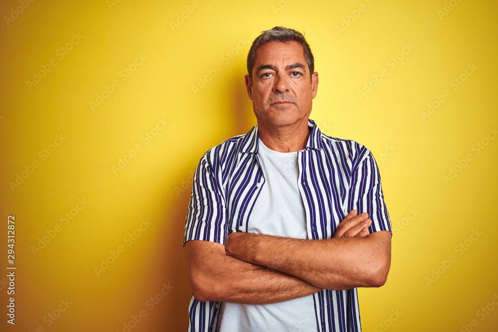 Handsome middle age man wearing striped shirt standing over isolated yellow background skeptic and nervous, disapproving expression on face with crossed arms. Negative person. Handsome middle age man wearing striped shirt standing over isolated yellow background skeptic and nervous, disapproving expression on face with crossed arms. Negative person.