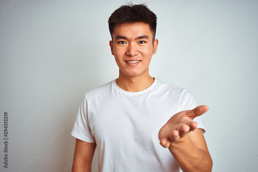 Young asian chinese man wearing t-shirt standing over isolated white background smiling cheerful offering palm hand giving assistance and acceptance. Young asian chinese man wearing t-shirt standing over isolated white background smiling cheerful offering palm hand giving assistance and acceptance.